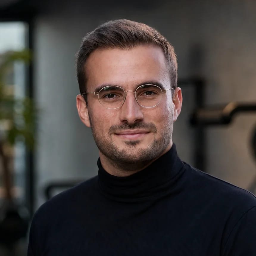 Carl, founder of Bespoke Fit, in a dark turtleneck and round glasses, a gym softly out of focus behind him.